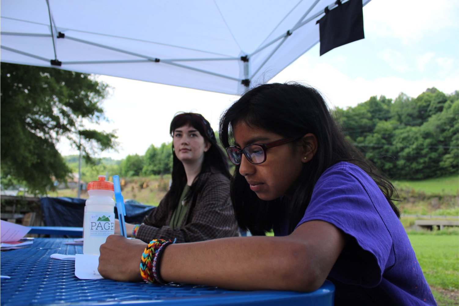 PAGE girls writing outdoors under a tent