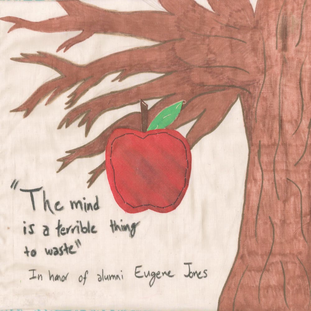 A quilt square depicting a large tree and an apple. Written on it is the quote 